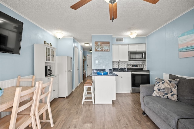 kitchen featuring appliances with stainless steel finishes, a breakfast bar area, white cabinets, ornamental molding, and light hardwood / wood-style floors