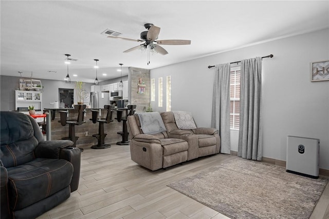 living room featuring a ceiling fan, baseboards, visible vents, and light wood-type flooring