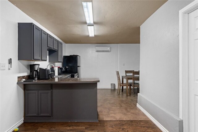 kitchen with dark countertops, freestanding refrigerator, a peninsula, an AC wall unit, and gray cabinetry