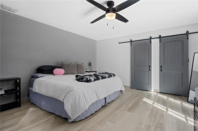 bedroom featuring a ceiling fan, visible vents, light wood-style flooring, and a barn door