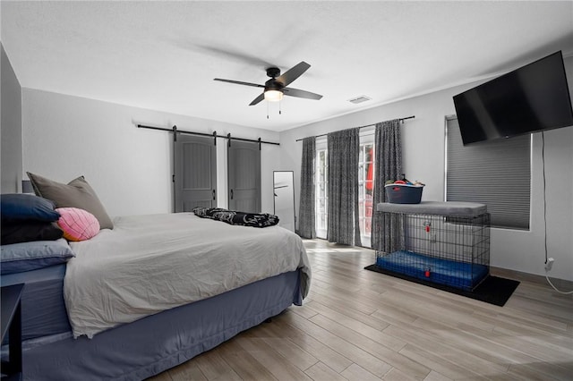 bedroom with ceiling fan, visible vents, light wood-style floors, and a barn door