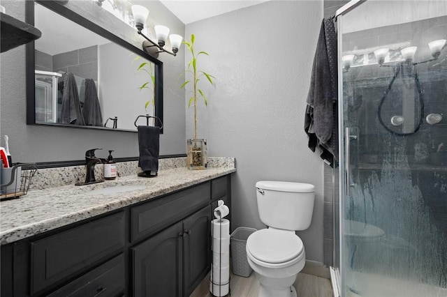 full bath featuring wood finished floors, a stall shower, vanity, baseboards, and toilet