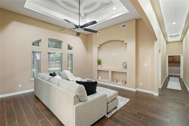 living area featuring visible vents, a tray ceiling, arched walkways, and dark wood-style floors