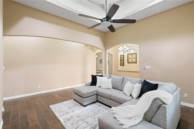 living room featuring ceiling fan, arched walkways, dark wood-style flooring, and baseboards