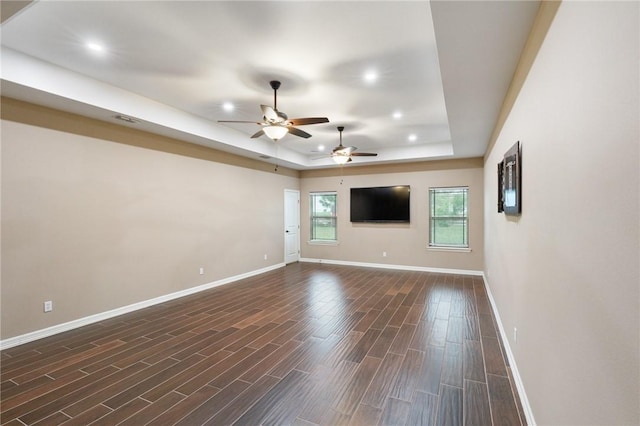 unfurnished living room featuring baseboards, a ceiling fan, a tray ceiling, and dark wood-style floors