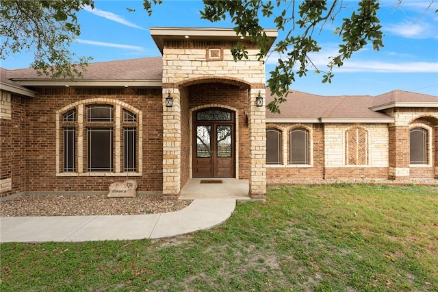 property entrance with a lawn, french doors, brick siding, and roof with shingles