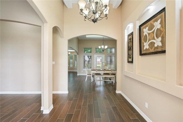entryway featuring a chandelier, arched walkways, baseboards, a high ceiling, and dark wood-type flooring