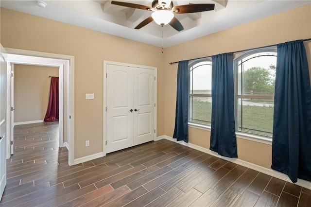unfurnished bedroom with a closet, ceiling fan, baseboards, a raised ceiling, and wood finish floors