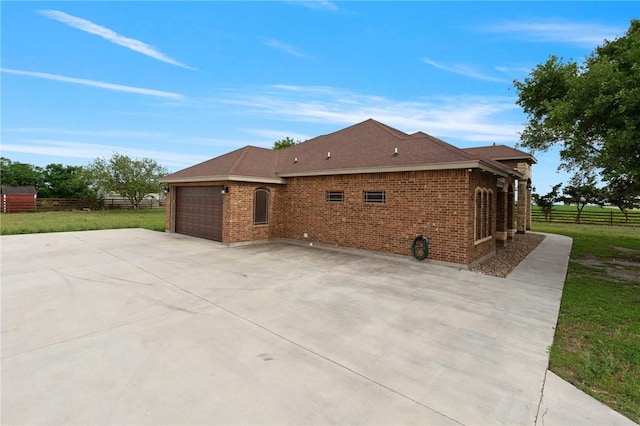 view of side of home with an attached garage, brick siding, fence, and driveway