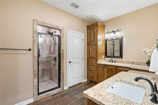 full bathroom with a sink, wood tiled floor, a stall shower, double vanity, and baseboards