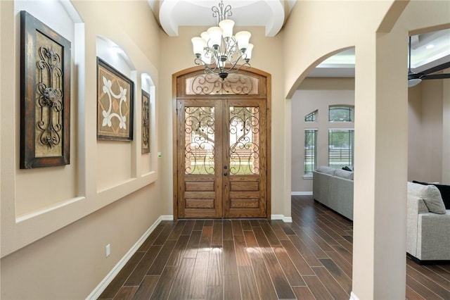 foyer with baseboards, dark wood-style floors, arched walkways, and a chandelier