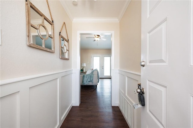 corridor featuring dark wood-style floors, a wainscoted wall, visible vents, a decorative wall, and ornamental molding