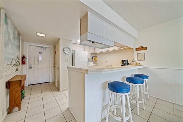 14810 Windward Dr Unit 301, Corpus Christi, TX 78418 - kitchen featuring freestanding refrigerator, light tile patterned floors, a peninsula, a breakfast bar area, and a textured ceiling
