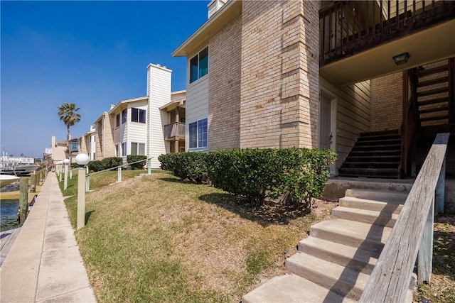 view of property exterior with stairway, a water view, brick siding, and a yard