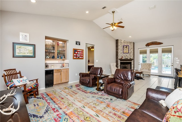 living room featuring ceiling fan, light tile patterned floors, high vaulted ceiling, a stone fireplace, and bar area