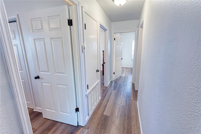 hall with a textured wall, dark wood finished floors, visible vents, and baseboards