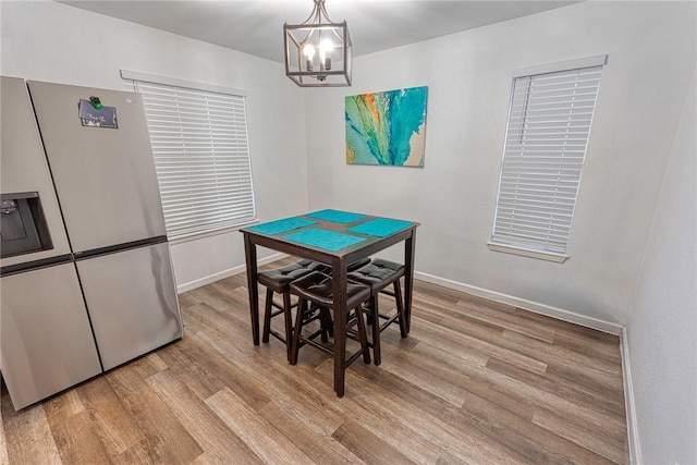 dining space featuring light wood-style flooring, baseboards, and a notable chandelier