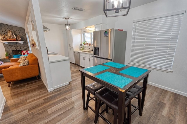 dining space featuring a stone fireplace, wood finished floors, visible vents, and baseboards