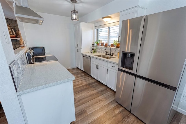 kitchen featuring wood finished floors, a sink, white cabinetry, wall chimney range hood, and appliances with stainless steel finishes