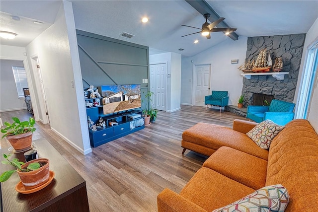 living area featuring baseboards, visible vents, lofted ceiling with beams, wood finished floors, and a stone fireplace