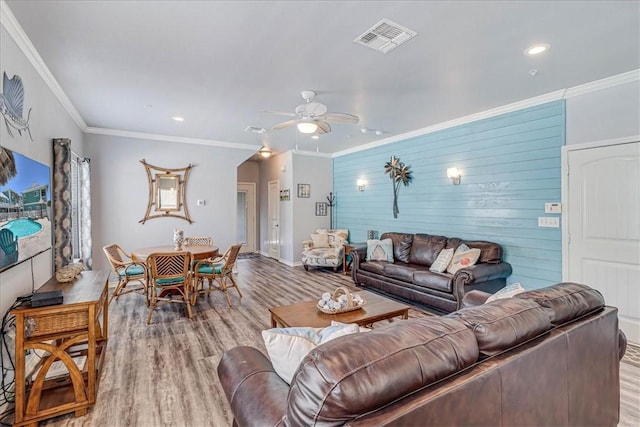 living room featuring ornamental molding, light hardwood / wood-style floors, ceiling fan, and wood walls