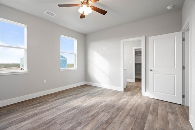 unfurnished bedroom featuring a closet, a walk in closet, light hardwood / wood-style floors, and ceiling fan