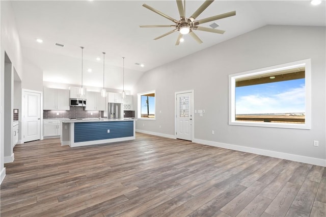 kitchen featuring hanging light fixtures, an island with sink, lofted ceiling, white cabinets, and appliances with stainless steel finishes