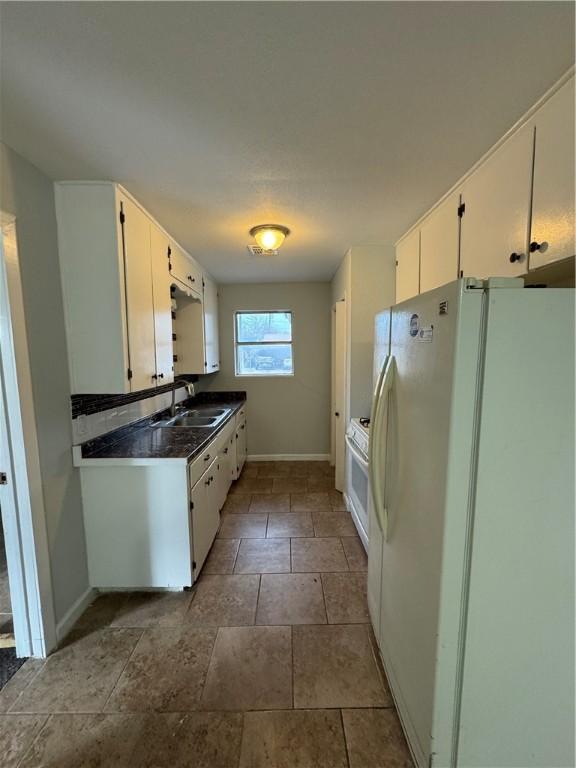 kitchen with a sink, dark countertops, white cabinetry, white appliances, and baseboards