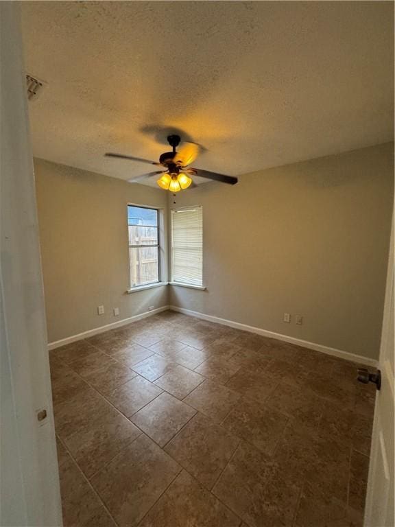 spare room featuring dark tile patterned floors, ceiling fan, a textured ceiling, and baseboards