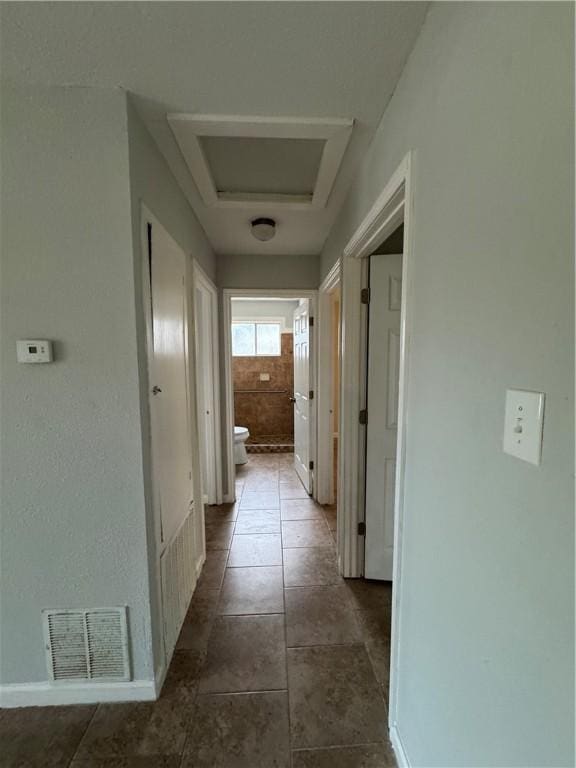 hall with dark tile patterned floors, visible vents, attic access, and baseboards