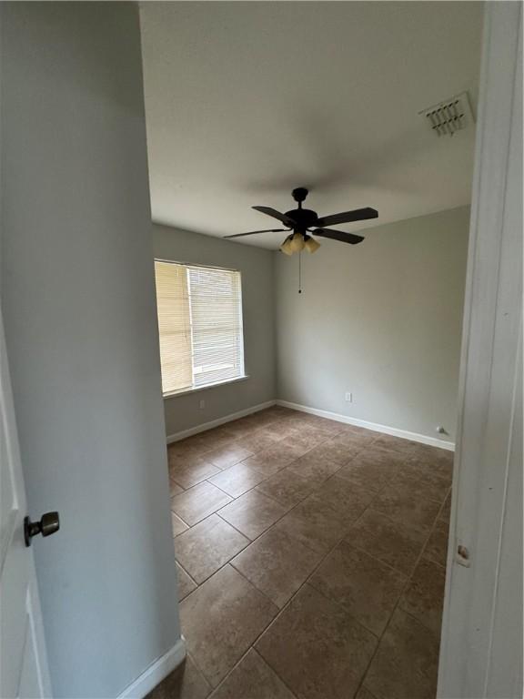 spare room with visible vents, baseboards, dark tile patterned flooring, and a ceiling fan