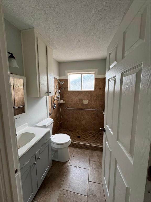 bathroom featuring vanity, a stall shower, tile patterned flooring, a textured ceiling, and toilet