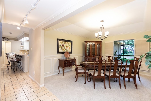 carpeted dining room with an inviting chandelier, sink, track lighting, and crown molding