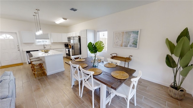 dining area with light wood-type flooring, visible vents, and baseboards