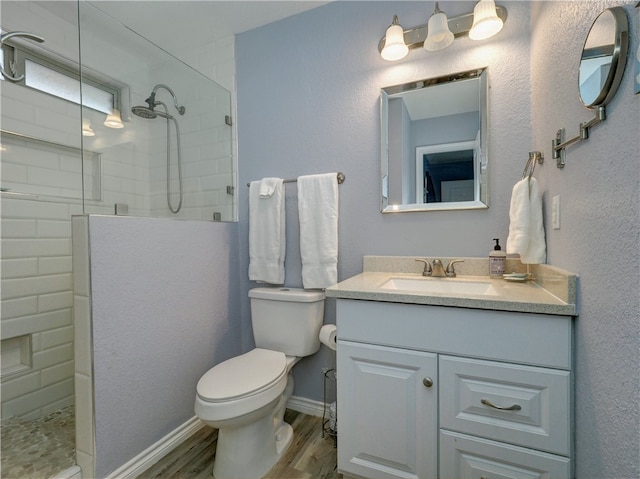 bathroom with hardwood / wood-style flooring, vanity, toilet, and tiled shower