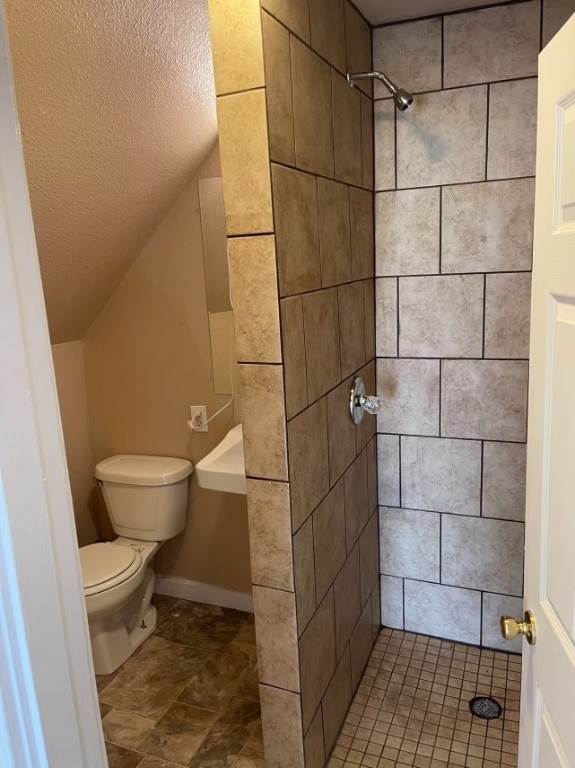 bathroom with toilet, tiled shower, and vaulted ceiling