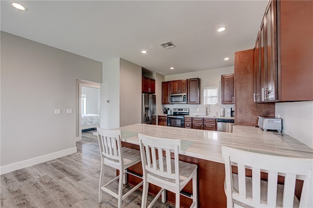 kitchen featuring a kitchen breakfast bar, kitchen peninsula, light hardwood / wood-style floors, and stainless steel appliances