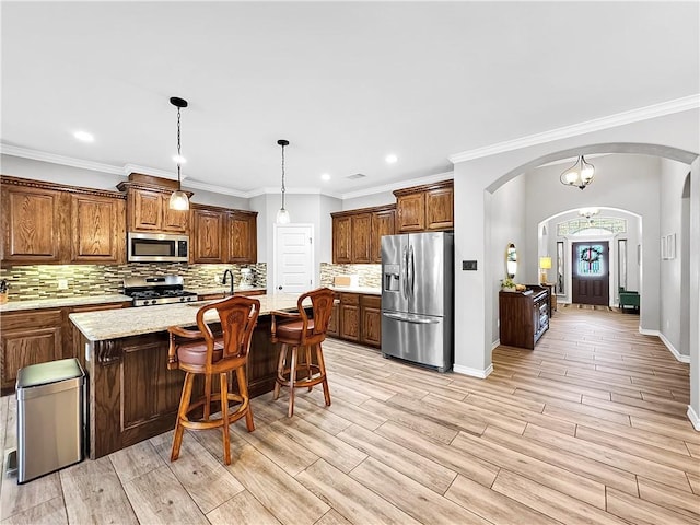 kitchen featuring stainless steel appliances, tasteful backsplash, light stone counters, a kitchen island with sink, and a breakfast bar