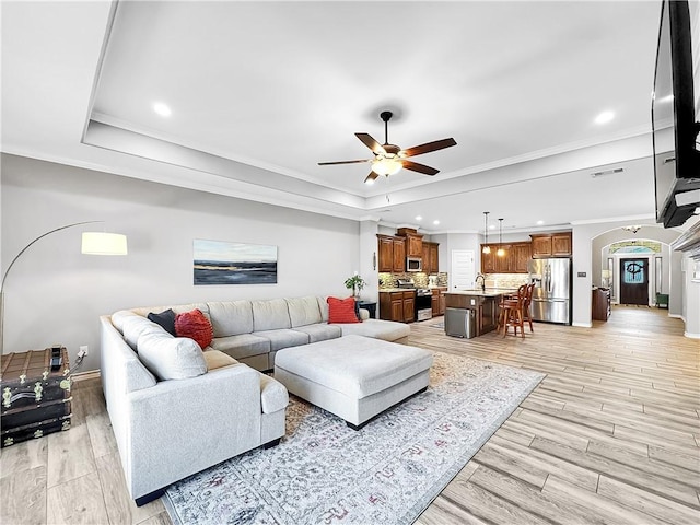 living room with ceiling fan, a raised ceiling, and crown molding