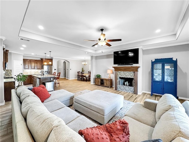 living room featuring a fireplace, ceiling fan with notable chandelier, light hardwood / wood-style floors, and a raised ceiling