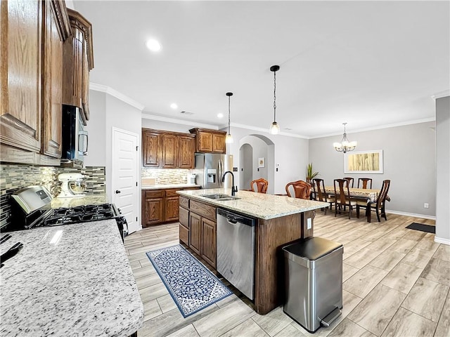 kitchen featuring light stone counters, backsplash, pendant lighting, a kitchen island with sink, and appliances with stainless steel finishes