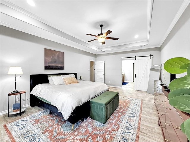 bedroom featuring light wood-type flooring, a tray ceiling, ceiling fan, crown molding, and a barn door