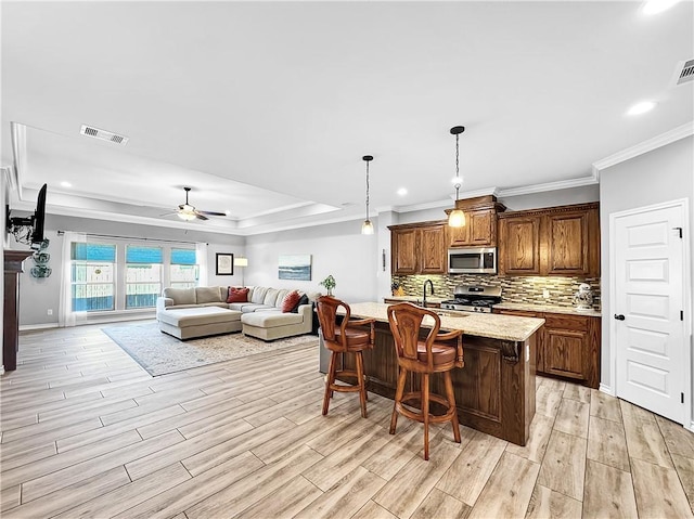 kitchen with appliances with stainless steel finishes, a breakfast bar, ceiling fan, hanging light fixtures, and an island with sink