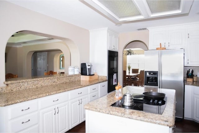 kitchen featuring black appliances, crown molding, a kitchen island, white cabinetry, and light stone countertops