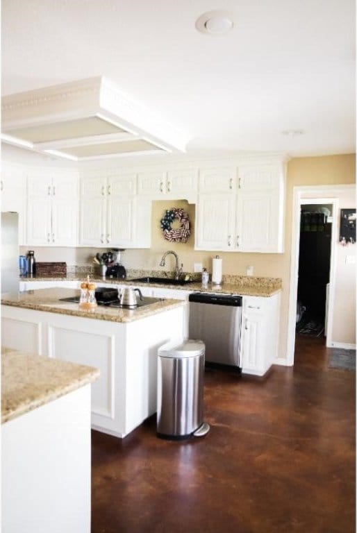 kitchen with light stone counters, dishwasher, sink, a kitchen island, and white cabinetry