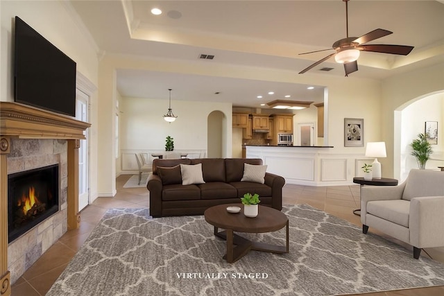 6825 Old Square Dr, Corpus Christi, TX 78414 - tiled living area featuring a tray ceiling, arched walkways, a fireplace, a decorative wall, and ceiling fan