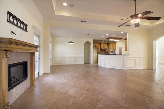6825 Old Square Dr, Corpus Christi, TX 78414 - unfurnished living room featuring arched walkways, a tray ceiling, a decorative wall, a tiled fireplace, and a ceiling fan