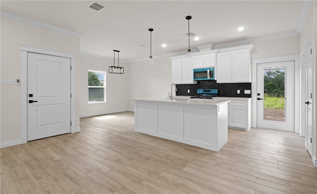 kitchen with appliances with stainless steel finishes, decorative light fixtures, white cabinetry, decorative backsplash, and a center island with sink