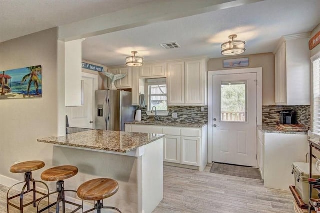 kitchen with tasteful backsplash, light stone counters, white cabinetry, stainless steel fridge with ice dispenser, and light hardwood / wood-style flooring