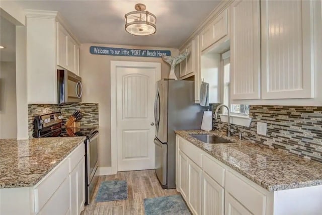 kitchen with white cabinets, light hardwood / wood-style flooring, sink, light stone countertops, and appliances with stainless steel finishes